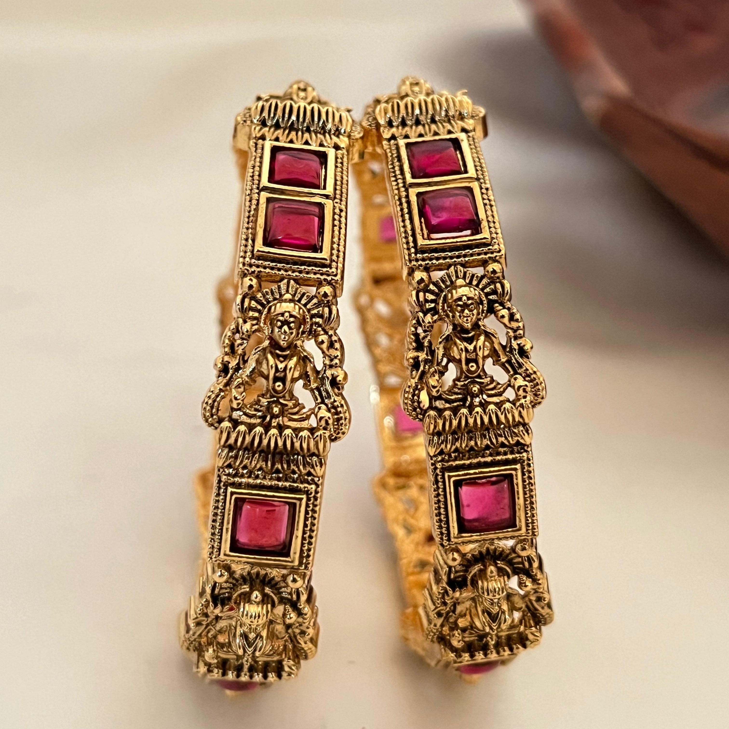 Ornate gold earrings with red gemstones on a light background