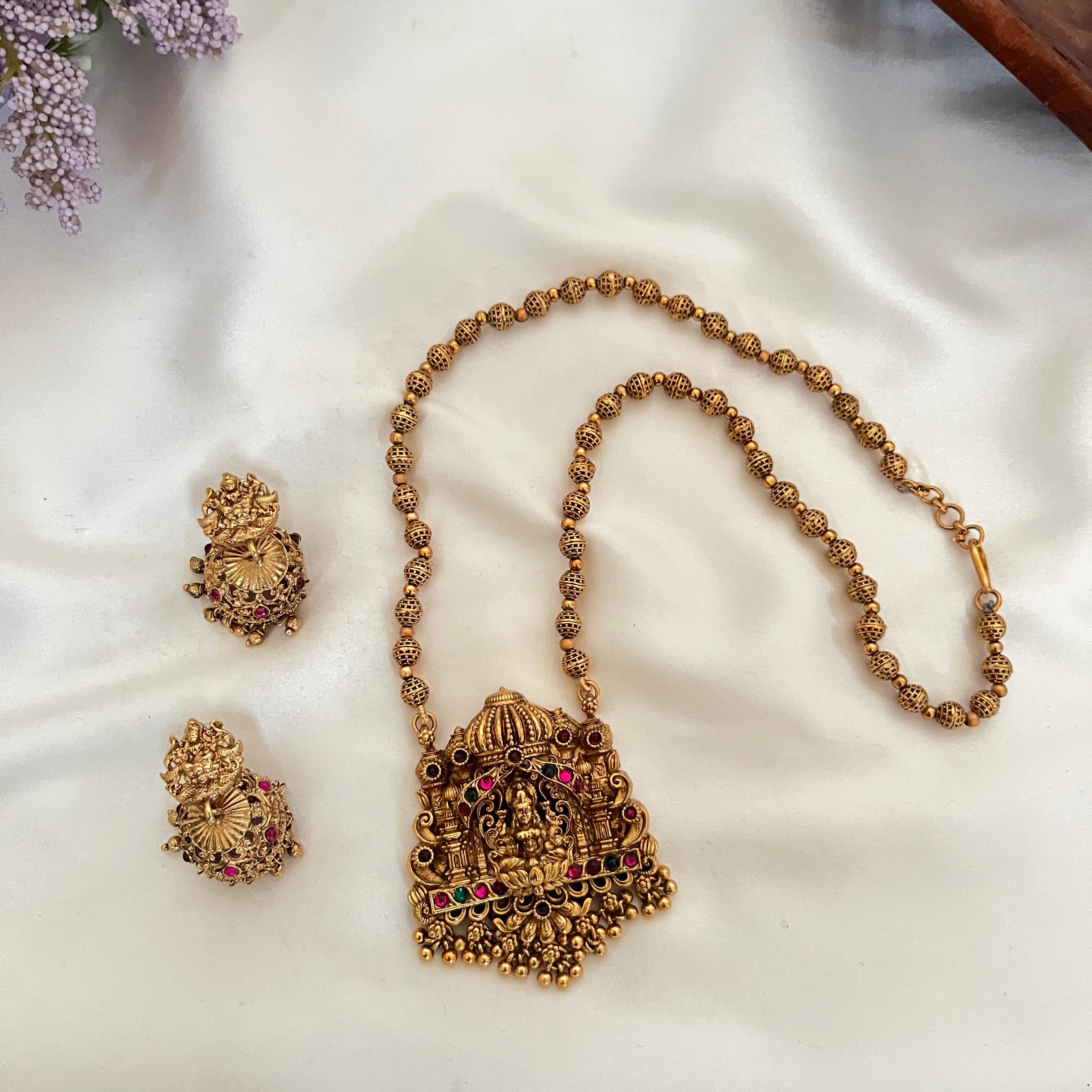 Gold necklace and earrings on a white fabric background with flowers and a wooden box.
